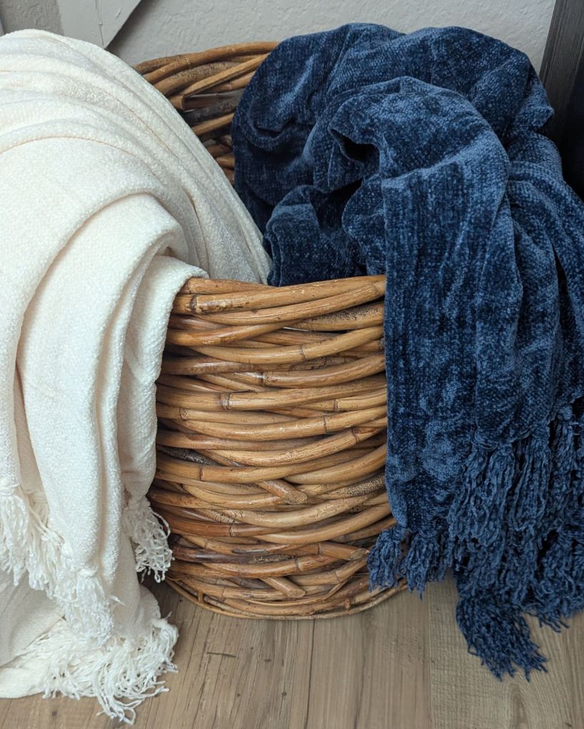 Woven wood basket holding cream and navy throw blankets in living room