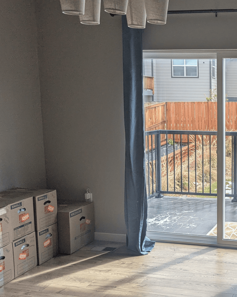 Unpacked moving boxes in a sunlit room with a sliding door open to the backyard, a home still coming together