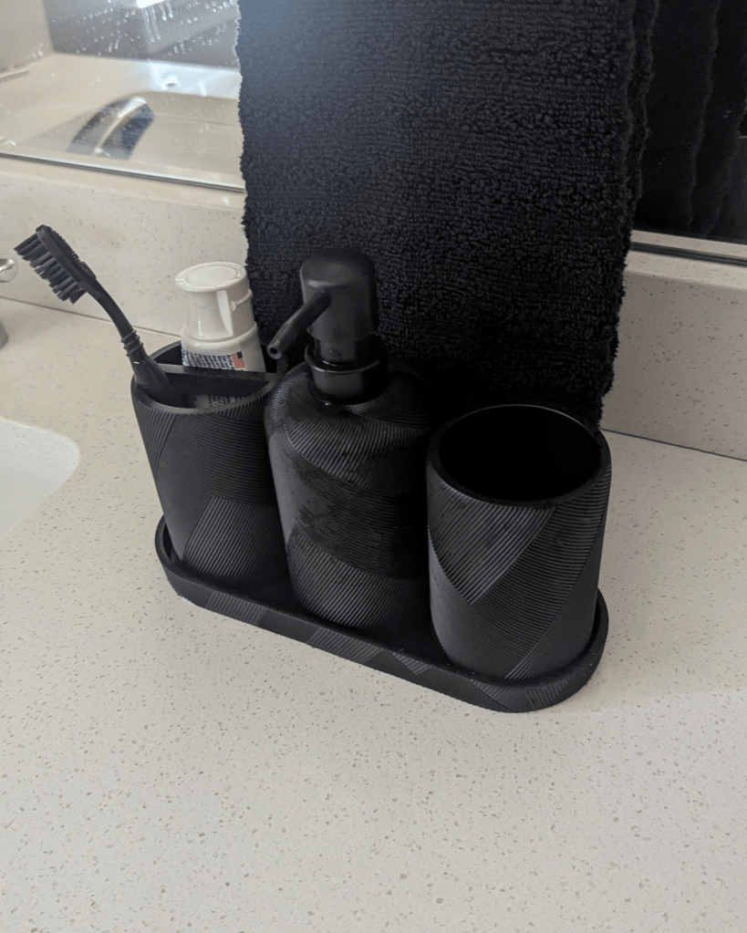 Matte black resin bathroom accessory set with soap dispenser and tumbler on a bathroom counter